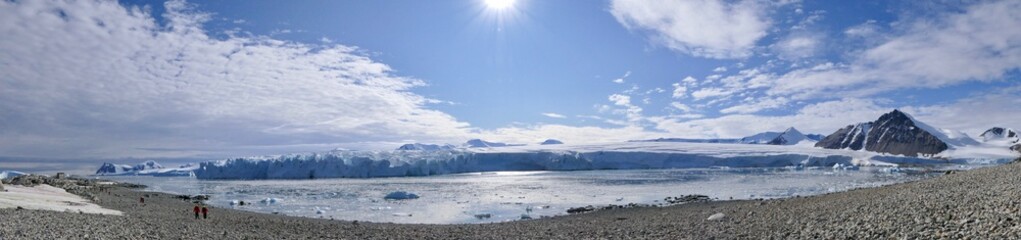 Fototapeta premium People on winter stone beach landscape with glacier front, ice floes and mountains and in Antarctica, Stonington Island