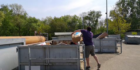 Plump,dark-haired,middle-aged man throws cardboard box with household waste into huge container at...