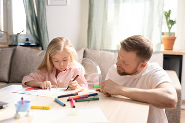 Happy young father in casualwear looking at his cute little daughter drawing