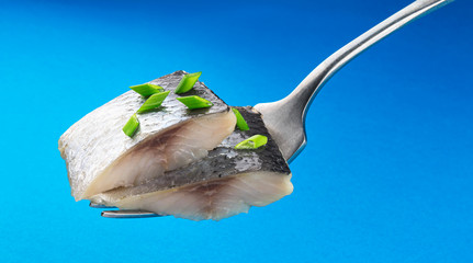 Pieces of salted herring on fork isolated on blue background