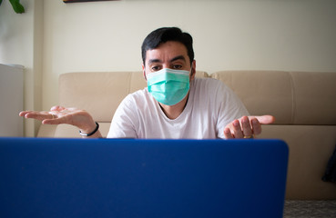 Caucasian man wearing a white T-shirt and a mask, dubitative, not knowing what's happening in the world on a video conference, while self-isolating due to the COVID-19 outbreak, in Spain