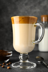 Closeup of Iced Dalgona coffee in glass mug on dark background. Trendy refreshment creamy whipped Macau coffee. Korean coffee drink. Vertical orientation