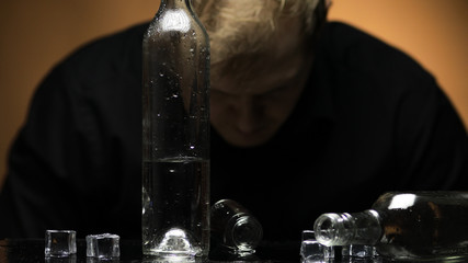 Depressed blurred man alcoholic. Vodka bottle and glasses on foreground