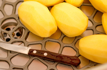 Raw peeled potatoes lie in the sink, washed under clean water. Cooking potatoes.