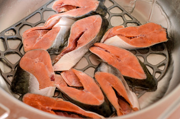 Salmon steaks lie in a metal sink, washed under water before cooking.