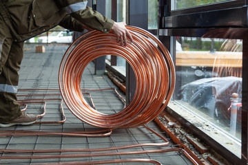 Plumber laying copper pipes on floor with warm heating