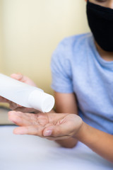 Young boy wearing mask is holding alcohol antiseptic gel bottle to clean hands and prevent germs.