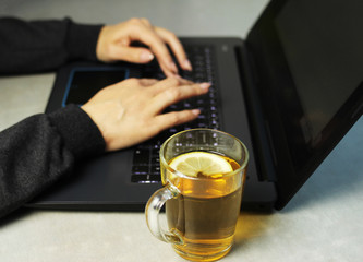 Young woman working on a laptop on the kitchen table and drinking lemon tea, remote work at home, self-isolation, selective focus