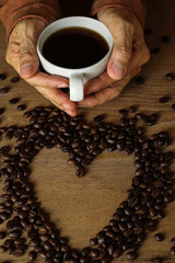 White coffee cup and coffee beans on wooden table with copyspace for text. Selective focus.