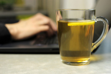 Young woman working on a laptop on the kitchen table and lemon tea, remote work at home, self-isolation, selective focus