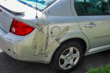 Damaged small gray car parked on a residential street. The rear panel is held on to car with...