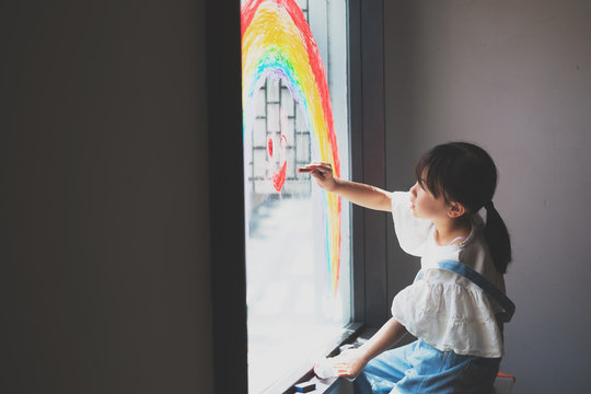 窓に虹の絵を描く少女