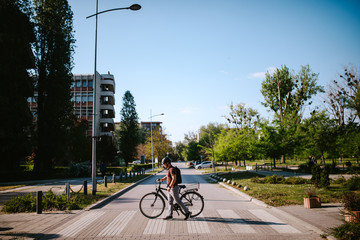 Handsome young caucasian man crosses pedestrian crossing and pushes bicycle
