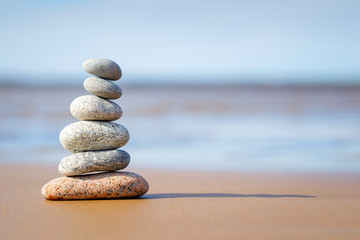 Pyramid stones balance on the sand of the beach. The object is in focus, the background is blurred.