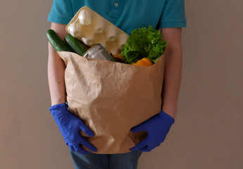 Volunteer in medical gloves delivers food in paper bag during virus outbreak, coronavirus pandemic.Front view