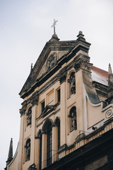 Antique baroque facade with window by decorative stucco on a beige wall with capitals and with sculptures of the Holy Fathers and the Blessed Virgin Mary in niches. Roof of Jesuit Church in Lviv.