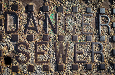 Close up photo of a danger sign on an old, rusty steel sewer grate.
