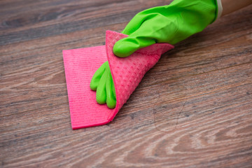 Closeup of a hand in a green rubber glove rubbing a wet wooden surface. The concept of disinfection of premises, the prevention of viral and bacterial diseases. Cleaning wooden surfaces.