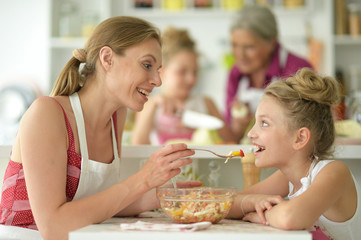 Portrait of cute little girl with her mother eating at kitchen table