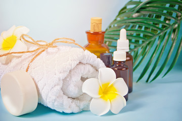 Fototapeta na wymiar Care, beauty and spa concept. Organic soap, small bottles with essential oils, white towel, palm leaf, plumeria frangipani flower.
