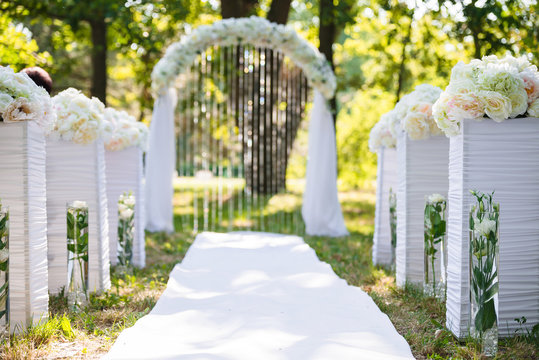 White luxury wedding ceremony decorations outdoor in the summer park. Table, chairs and weddinh decorated arch