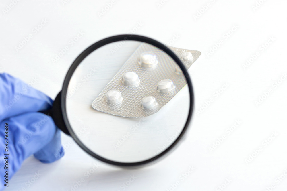 Wall mural Hand holds a magnifying glass over pills on a white background.