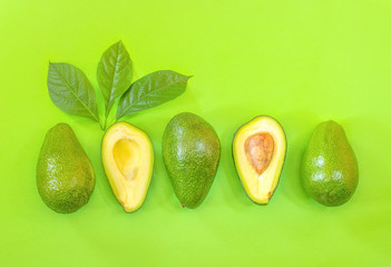 whole avocados and avocado halves with green leaves on a green background top view. background with...