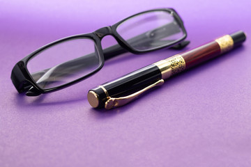 Stylish pen and glasses lie on a dark beautiful background.