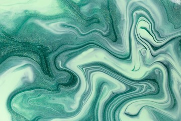 Abstract background of mixed shades of green nail polish with a pastel marble pattern. Liquid colorful background paint creative pastel cold green hue with shimmer