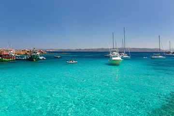 Obraz premium Various tourist boats are stationed in the clear and transparent waters in the Maddalena archipelago in Sardinia, Italy.