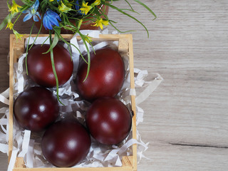 Easter painted eggs in a wooden stand and a bouquet of spring flowers on a light wooden background top view. Bright template for the Easter holiday