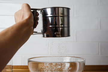 
metal sieve for flour in a female hand. Confectioner sifts flour before making dough