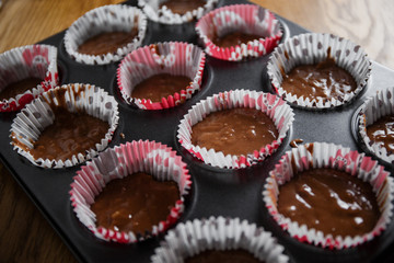 
A muffin baking dish in which there are paper inserts with chocolate dough inside. Homemade cakes for children and adults