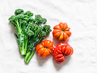Fresh heirloom tomatoes and broccoli on a light background, top view
