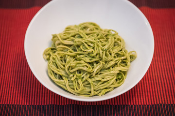 Homemade pasta noodles with green pesto on red background