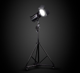 Photography studio flash on a lighting stand isolated on black background.