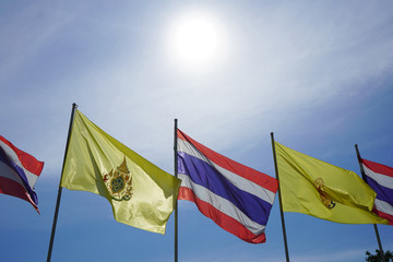 The sun is shining light over Thai national flags and His Majesty King Vajiralongkorn flags.