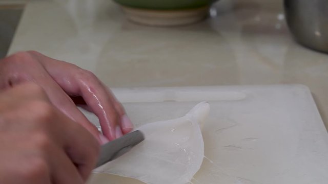 Knife in female hand cleans fresh squid on cutting board on home kitchen. Whiteraw seafood
