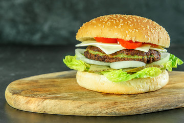 Vegetarian burger with spinach cutlet, onion, tomato, lettuce, cucumber and cheese on the wooden cutting board. Light tasty hamburger for vegetarians.