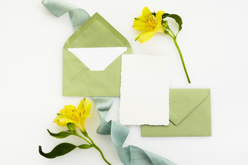 Blank white greeting card with envelope and flowerson white background. Top view. Mock up