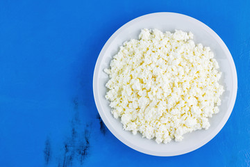 Cottage cheese in a white plate on a blue background. Organic eco healthy meal, dairy product. Plate of homemade cottage cheese. Top view. Copy space