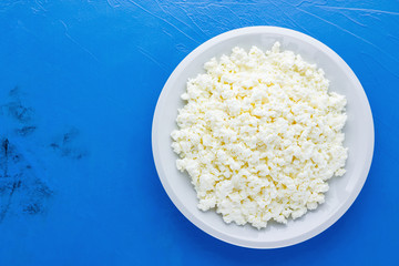 Cottage cheese in a white plate on a blue background. Organic eco healthy meal, dairy product. Plate of homemade cottage cheese. Top view. Copy space