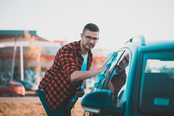 Portrait of a satisfied man cleaning his own car with a cloth.