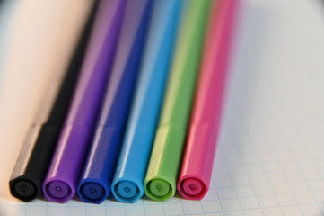 Close-Up Of Color Markers Against Blank Squared Notebook Sheet.