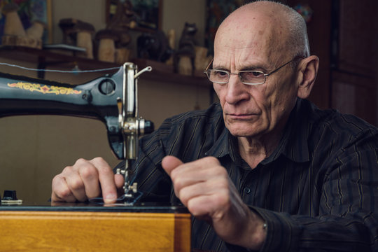 senior tailor with glasses sewing on black vintage machine tool on table