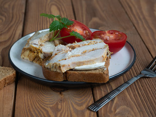 Fototapeta na wymiar Sandwich with chicken ham and sliced tomato on a ceramic plate on a wooden table