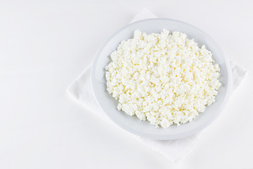 Cottage cheese in a plate on a white background. Cottage cheese on a white napkin. Top view. Copy space
