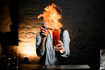 woman bartender holds glass with cocktail and sets fire to it