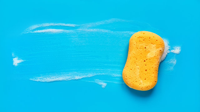 Yellow washing sponge in soap foam on a blue background isolated