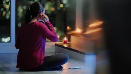 Girl doing yoga training at home at night. Young hispanic woman doing meditation using app software on smartphone. Healthy lifestyle and people meditating